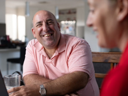 MSWA Client smiling at camera. MSWA staff in the foreground.