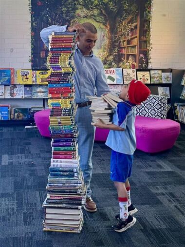 Boy stands to the right of a large tower of books he read for the Readathon.