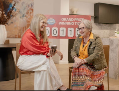 Two women sit in a luxury kitchen making a phone call