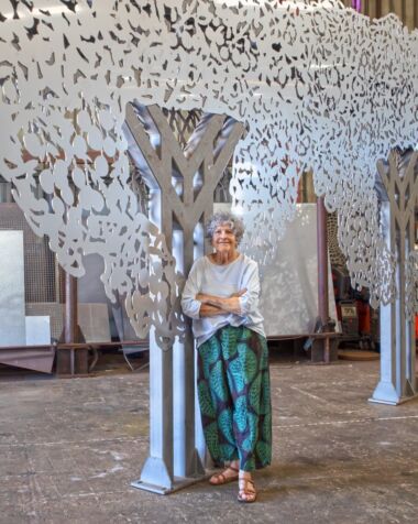 Lady standing next to a big steel work that resembles a tree.