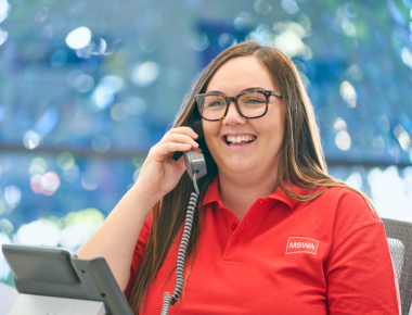 Women wearing a red MSWA shirt and speaking on the phone smiling
