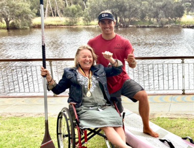 Woman in a wheelchair holding a paddle and smiling beside her son