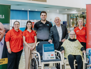 People at a pool standing next to a water wheelchair