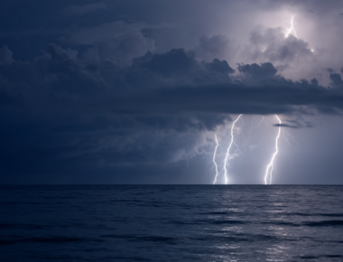 Lightning striking over ocean beneath dark storm clouds during a nighttime thunderstorm