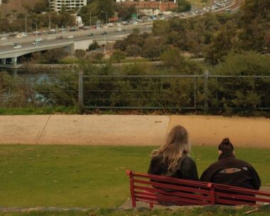 Two people sitting on a park bench looking over the Perth skyline.