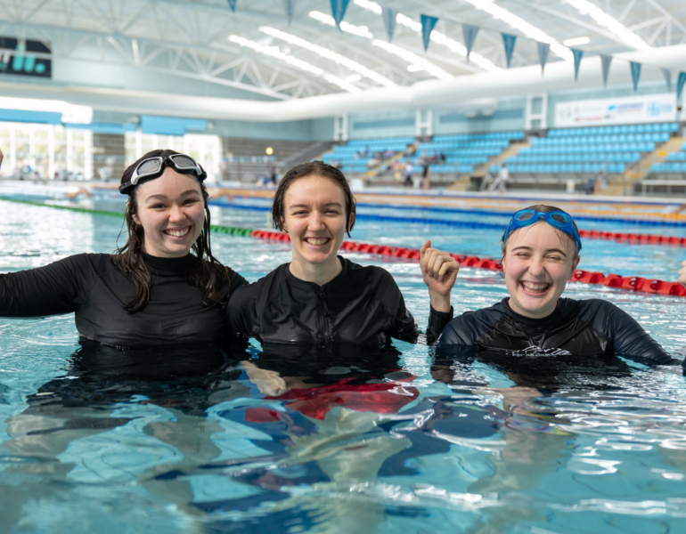 Three women in a pool celebrating and smiling.
