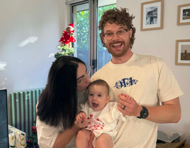 Dad holding baby and mum kissing baby forehead.