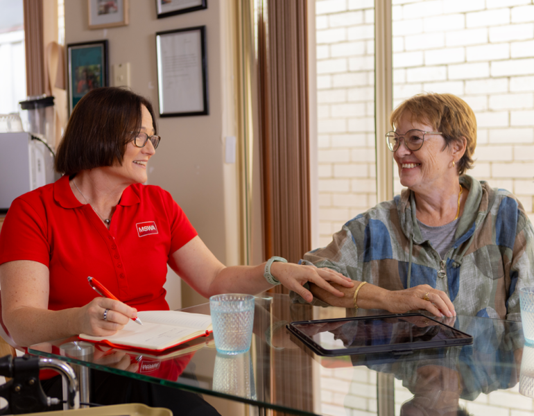 MSWA staff member and Jo smiling together at a table during a one-on-one counselling session