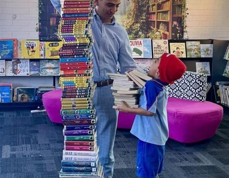 Boy stands to the right of a large tower of books he read for the Readathon.