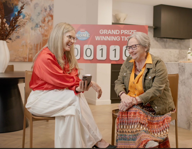 Two women sit in a luxury kitchen making a phone call