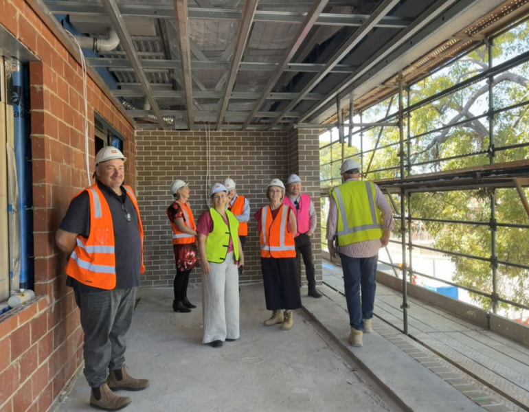 People wearing hi-vis and construction hats smiling to the camera at the MSWA Shenton Park construction site.