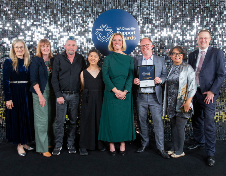 A group of people posing with their award against a sparkly backdrop