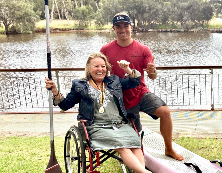 Woman in a wheelchair holding a paddle and smiling beside her son