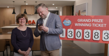 Anita stands on the left, Tony is on the right, as he holds a mobile phone, smiling, about to call the winner.
