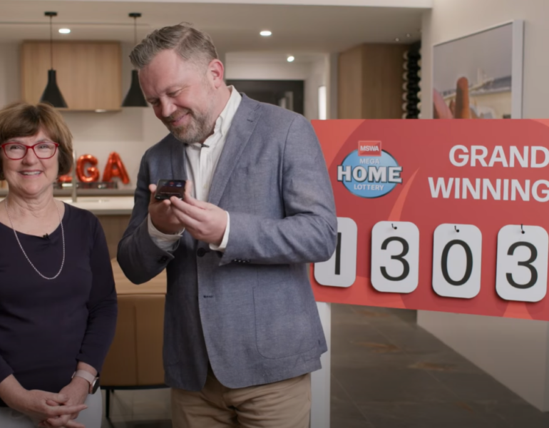 Anita stands on the left, Tony is on the right, as he holds a mobile phone, smiling, about to call the winner.