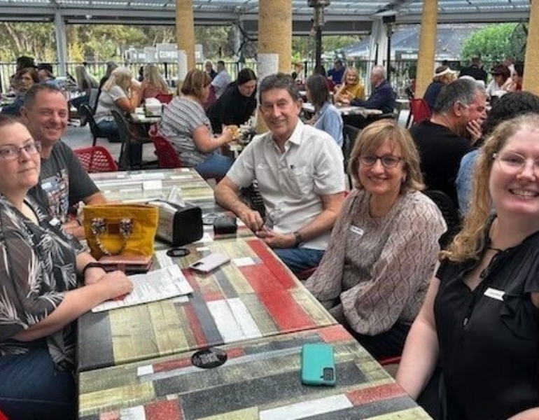 Group of people sitting around a table, looking at the camera and smiling