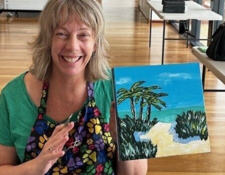 woman holding a painting and smiling at the camera