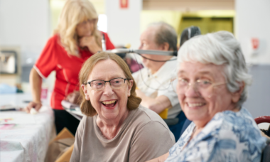 two women smiling at the camera in a social, community setting