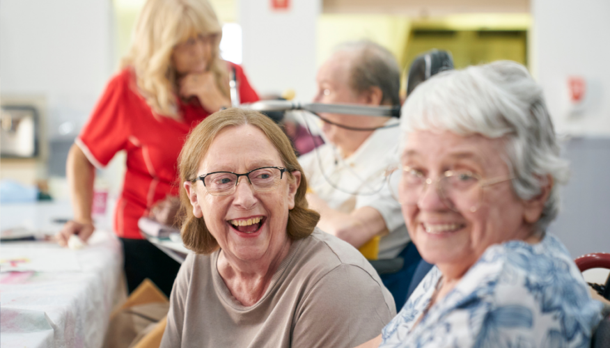 two women smiling at the camera in a social, community setting
