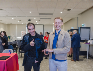 Man holding a device standing next to a man holding a thumbs up.