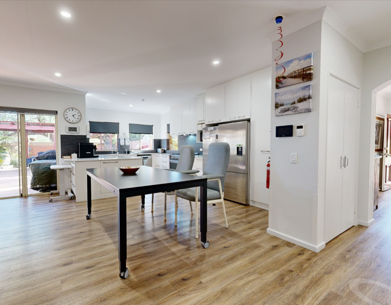 Kitchen with windows letting in sunlight. Table in the middle with two chairs situated next to it.
